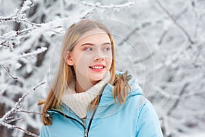 Beautiful happy teenage girl portrait walking outdoors on snowy white winter day in a snow forest