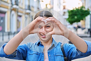 Beautiful happy teenage girl showing heart sign with hands, outdoor in the city