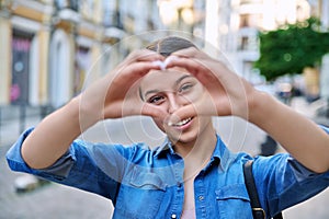 Beautiful happy teenage girl showing heart sign with hands, outdoor in the city