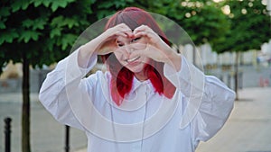 Beautiful happy teenage girl showing heart sign with hands, outdoor in the city