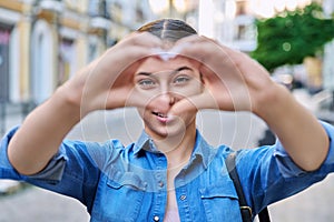 Beautiful happy teenage girl showing heart sign with hands, outdoor in the city