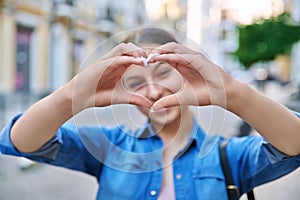 Beautiful happy teenage girl showing heart sign with hands, outdoor in the city