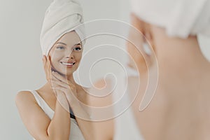 Beautiful happy woman after applying make up looking in mirror and smiling while standing in bathroom