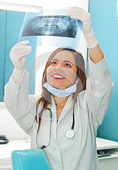 Beautiful happy woman doctor holding a X-Ray and watching teeth structure at dentist`s office