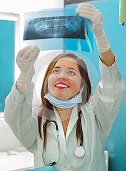 Beautiful happy woman doctor holding a X-Ray and watching teeth structure at dentist`s office