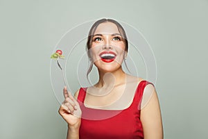 Beautiful happy woman eating healthy food holding fork with tomatoes and lettuce on white background. Healthy eating and diet