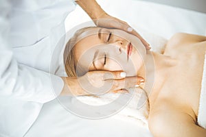 Beautiful happy woman enjoying facial massage with closed eyes in spa salon. Relaxing treatment in medicine and Beauty