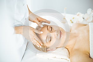 Beautiful happy woman enjoying facial massage with closed eyes in spa salon. Relaxing treatment in medicine and Beauty