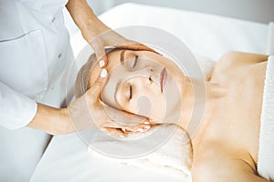 Beautiful happy woman enjoying facial massage with closed eyes in spa salon. Relaxing treatment in medicine and Beauty