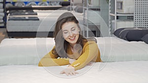 Beautiful happy woman examining orthopedic mattress on sale