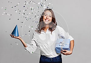 Beautiful happy woman with gift box at celebration party with confetti falling everywhere on her.