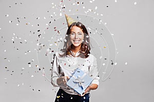 Beautiful happy woman with gift box at celebration party with confetti falling everywhere on her.