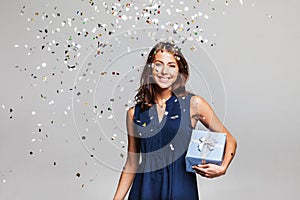 Beautiful happy woman with gift box at celebration party with confetti falling everywhere on her.