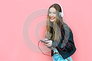 Beautiful happy woman in headphones listening music near the wall