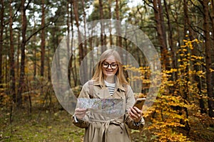 Beautiful happy woman holding mobile phone using map to navigate in autumn forest. Happy tourist trying to find best way