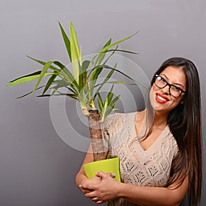 Beautiful happy woman holding plant in vase against gray background