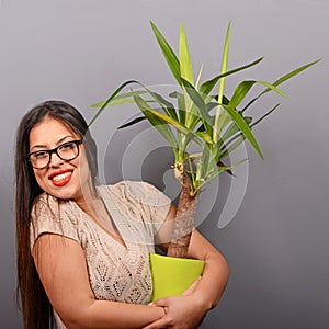 Beautiful happy woman holding plant in vase against gray background