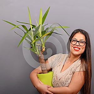 Beautiful happy woman holding plant in vase against gray background