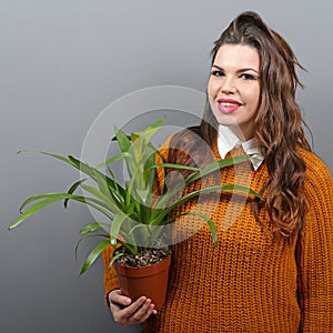 Beautiful happy woman holding plant in vase against gray background