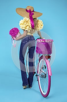 Beautiful happy woman in jeans and big hat with colorful bike decorated with flowers. Spring fashion concept