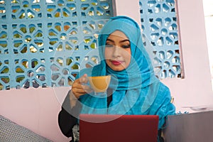 Beautiful and happy woman in muslim hijab head scarf working with laptop computer or having fun networking using the internet at r