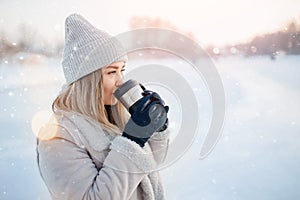 Beautiful happy woman outdoor winter. Laughing girl with hot drink tea or coffee with snowfall