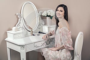 Beautiful happy woman with pink dress and long black hair in her room near her dressing table posing before party.