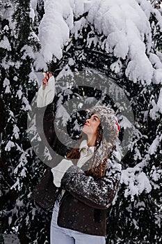 Beautiful happy woman portrait at snowy forest. Young Lady enjoying snow falling from spruce branches