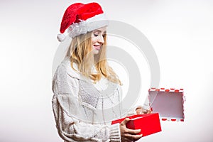Beautiful happy woman in red Santa hat and beige sweater opens her Christmas gift, box with ribbon