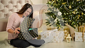 Beautiful Happy Woman Sitting Next To Christmas Tree With A Gift In Her Hands. Merry Christmas and New Year Concept.