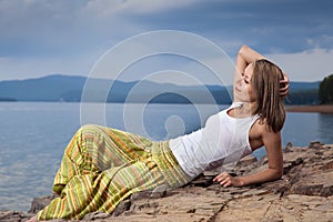 Beautiful happy woman sitting on rock over sea