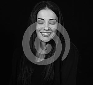 Beautiful happy woman with toothy smile and closed eyes making a wish on black background with empty space. Closeup portrait