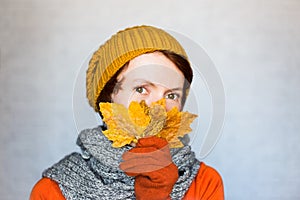 Beautiful happy woman wearing knitted clothes holds autumn yellow leaves near the face.