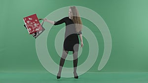 Beautiful happy woman wearing little black dress is posing and spinning with shopping bags. She is standing in a studio