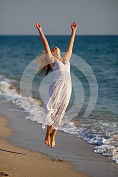 Beautiful happy woman in white dress jumping up on the beach on a Sunny day