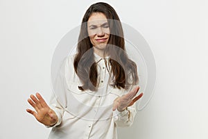 A beautiful, happy, woman in a white shirt on a light background stands smiling pleasantly, closing her eyes and showing