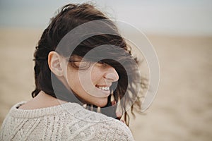 Beautiful happy woman with windy hair portrait on background of sandy beach and sea, carefree tranquil moment. Stylish young