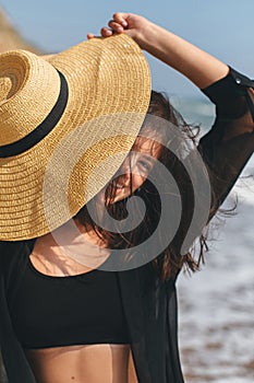 Beautiful happy woman with windy hair relaxing and smiling under hat on sandy beach at sea. Summer vacation.Stylish fit young