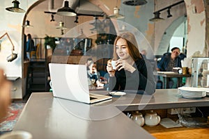 Beautiful happy woman working on laptop computer during coffee break in cafe bar