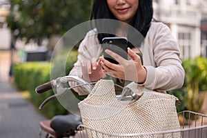 A beautiful, happy young Asian woman in a cute dress is using her smartphone on her bike in the city
