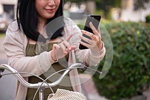 A beautiful, happy young Asian woman in a cute dress is using her smartphone on her bike in the city