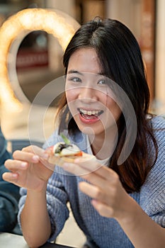 A beautiful and happy young Asian woman enjoying eating food at a restaurant with her friends