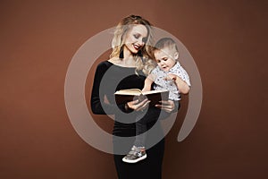 Beautiful and happy young blonde woman in the fashionable black dress with a cute little baby boy on her hands reading