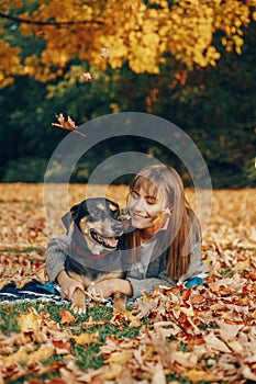 Beautiful happy young Caucasian woman sitting on ground among autumn fall yellow leaves and hugging her pet dog