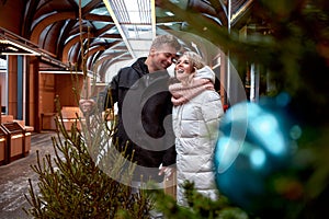 Beautiful happy young couple in love in Christmas market. Man and woman in winter clothes buying Christmas tree to