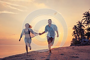 Beautiful happy young couple in love runs along the beach along the sand by the sea at sunset during a honeymoon holiday vacation