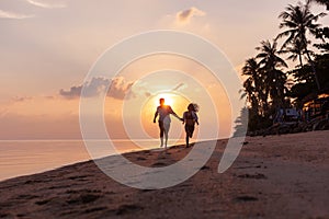 Beautiful happy young couple in love runs along the beach along the sand by the sea at sunset during a honeymoon holiday vacation