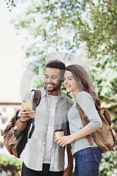 Beautiful happy young couple using smartphone outdoors. Joyful smiling woman and man looking at mobile phone in a city