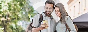 Beautiful happy young couple using smartphone outdoors panoramic banner. Joyful smiling woman and man looking at mobile phone in a