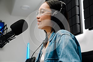 Beautiful happy young female radio host broadcasting in studio